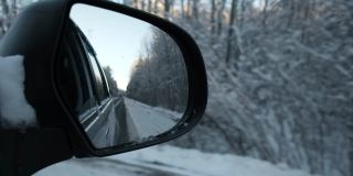 侧视镜反射冬季森林道路。风景与空荡的公路穿过白雪森林。汽车在道路上超速行驶。汽车在运动。旅游、旅游、旅行的概念。冰雪覆盖的树木。