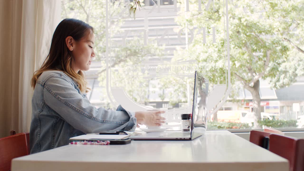 一个迷人的年轻女子坐在咖啡店里使用笔记本电脑的4k视频片段