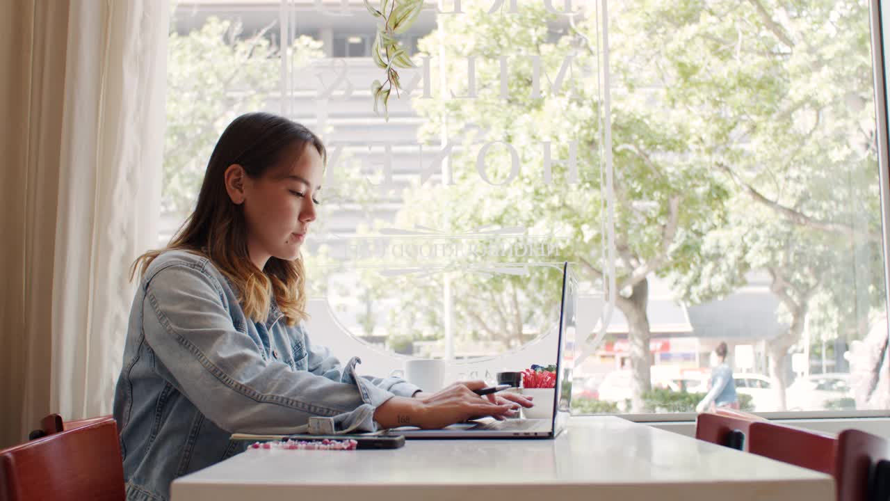一个迷人的年轻女子坐在咖啡店里使用笔记本电脑的4k视频片段