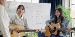 在一所音乐学校的课堂上，一位年轻的亚洲音乐老师正在教学生读乐谱和正确的吉他和弦