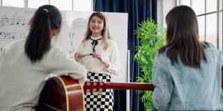 在一所音乐学校的课堂上，一位年轻的亚洲音乐老师正在教学生读乐谱和正确的吉他和弦