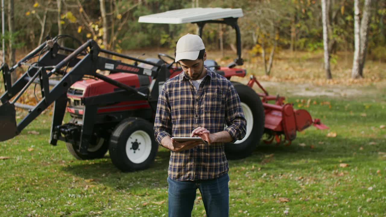 秋天的一天，一个年轻人站在农机旁，正在使用平板电脑