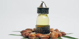 东方玻璃和金属瓶里的摩洛哥坚果油和白色背景上绿色叶子的摩洛哥坚果
