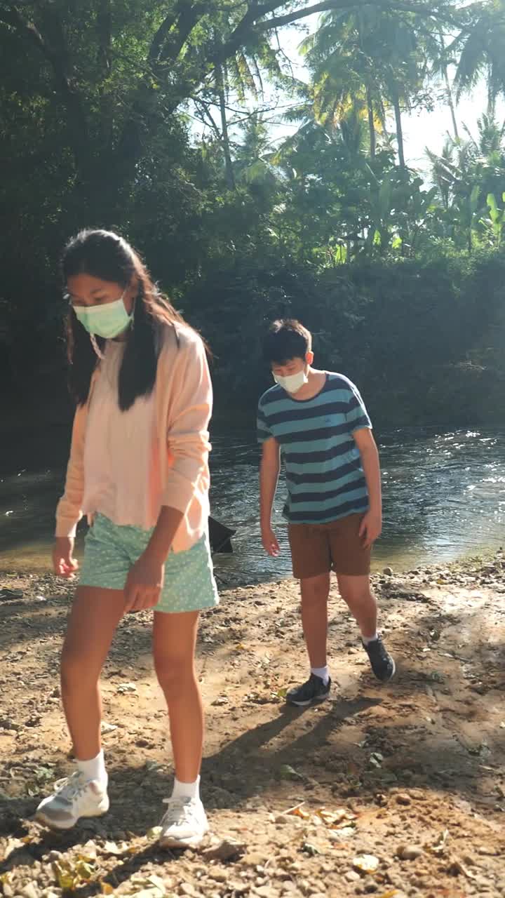 亚洲儿童戴着口罩一起在河边户外散步，生活理念。