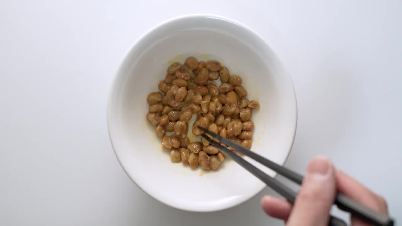 用慢镜头在白色碗里搅拌纳豆(发酵的日本大豆)