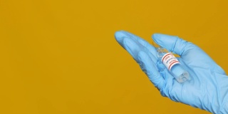 一名医生戴着一副黄色背景的手套，手上拿着一种抗冠状病毒Covid-19的疫苗。左边是一个复制空间。大流行期间的药物。强制接种Covid -19疫苗。