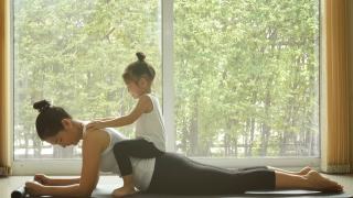 4 k。亚洲妈妈在家里练习瑜伽，有一个可爱的女儿坐在妈妈背上。隔离自我隔离期间的培训。休闲健康的生活方式。健康的家庭在早晨的活动视频素材模板下载