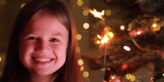 可爱的小女孩附近的圣诞树树枝与孟加拉灯的背景闪闪发光的花环。快乐小孩许下新年愿望，等待圣诞老人和奇迹。快乐的童年