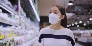 亚洲女性家庭主妇拉着手推车在商场超市挑选商品，女性戴着口罩在商场商店里行走寻找消费品