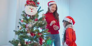 亚洲可爱的家庭，母亲和孩子女儿装饰圣诞树。年幼的女儿兴高采烈地和父母一起在家里庆祝节日圣诞感恩节派对