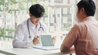 亚洲医生在诊所与病人交谈，同时使用平板电脑解释病人的情况和治疗结果。视频素材模板下载