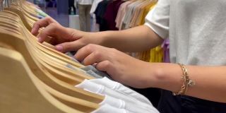 女人用手整理了许多衣架上的服装。在商店挑选和购买衣服。购物
