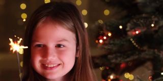 可爱的小女孩在家附近的圣诞树拿孟加拉灯的背景闪闪发光的花环。快乐小孩许下新年愿望，等待圣诞老人和奇迹。快乐的童年