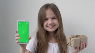 可爱的小女孩用绿色屏幕展示手机模拟手机、手机、电话和礼物。绿屏智能手机的色度键设置为广告。圣诞节，情人节，爱，母亲节视频素材模板下载