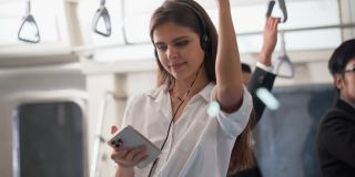 一名年轻女性乘客站在地铁上用智能手机听音乐。
