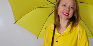 一个穿着黄色雨衣的女孩在伞下伸出手去淋雨。孤立在白色背景上