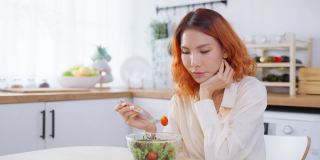 亚洲有吸引力的女人在家里厨房的桌子上吃绿色沙拉。年轻美丽的素食女孩感到快乐，享受早餐蔬菜健康的食物，在家里减肥健康。