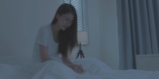 穿着睡衣的亚洲生病女孩在床上打喷嚏。有吸引力的年轻女子感觉不好，遭受过敏，把纸巾盖住她的鼻子，而在睡觉时打喷嚏在房子。