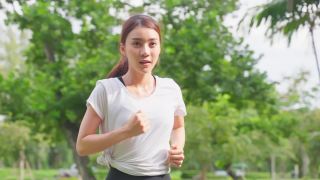 亚洲年轻美丽的运动女子在公园的街道上跑步。美丽的运动员和坚定的女孩在运动服装锻炼慢跑锻炼户外保健在傍晚日落在花园。视频素材模板下载