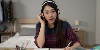 戴着耳机在家学习的亚洲女性学生的正面形象是在网上上课时重复句子和写笔记