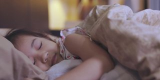 靠近可爱的5岁亚洲女孩的脸，她正在舒适地睡觉，在平静的灯光下在她的床上醒来，展示了童年的休息概念与甜蜜的梦和放松的夜晚。