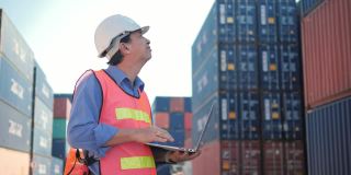 一个亚洲工头在安全帽和安全背心谈论无线电控制装载集装箱从货物装运