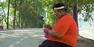 一个胖子坐在公园里喝水