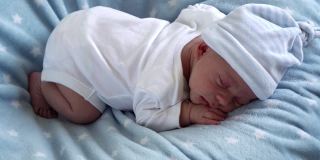 新生儿脸部特写，婴儿早期甜甜地睡在肚子上蓝色的星星背景。帽子上的孩子开始的时间。婴儿，分娩，出生的第一个时刻，开始概念