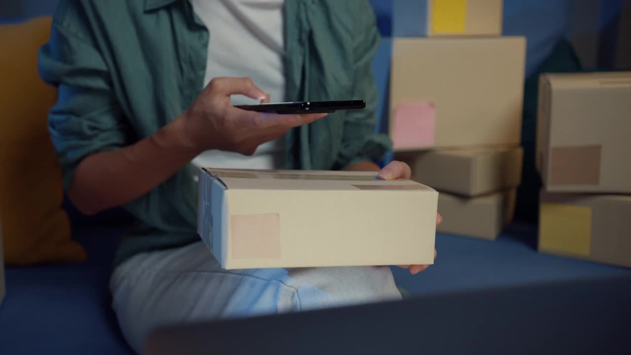 年轻的亚洲女销售员晚上在家里通过智能手机上的应用程序检查包裹箱是否要发货。