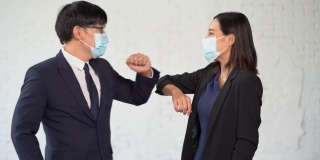 两名带着防护面罩的亚洲商人用肘撞来打招呼，而不是握手。在冠状病毒或Covid-19大流行期间，常见的问候用语