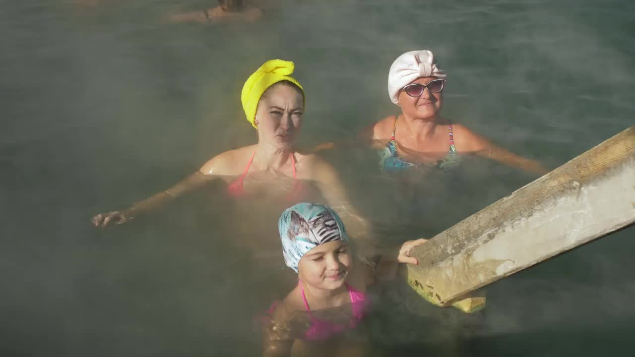 小女孩、妈妈和奶奶在一个传统的户外水疗中心游泳，有柔和的灯光和蒸汽。女孩女人放松