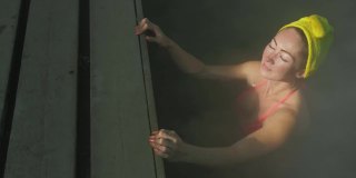 近距离的白人妇女在热盐水矿泉水浴在一个传统的温泉与软魔术粉红色照明蒸汽户外游泳。地热温泉