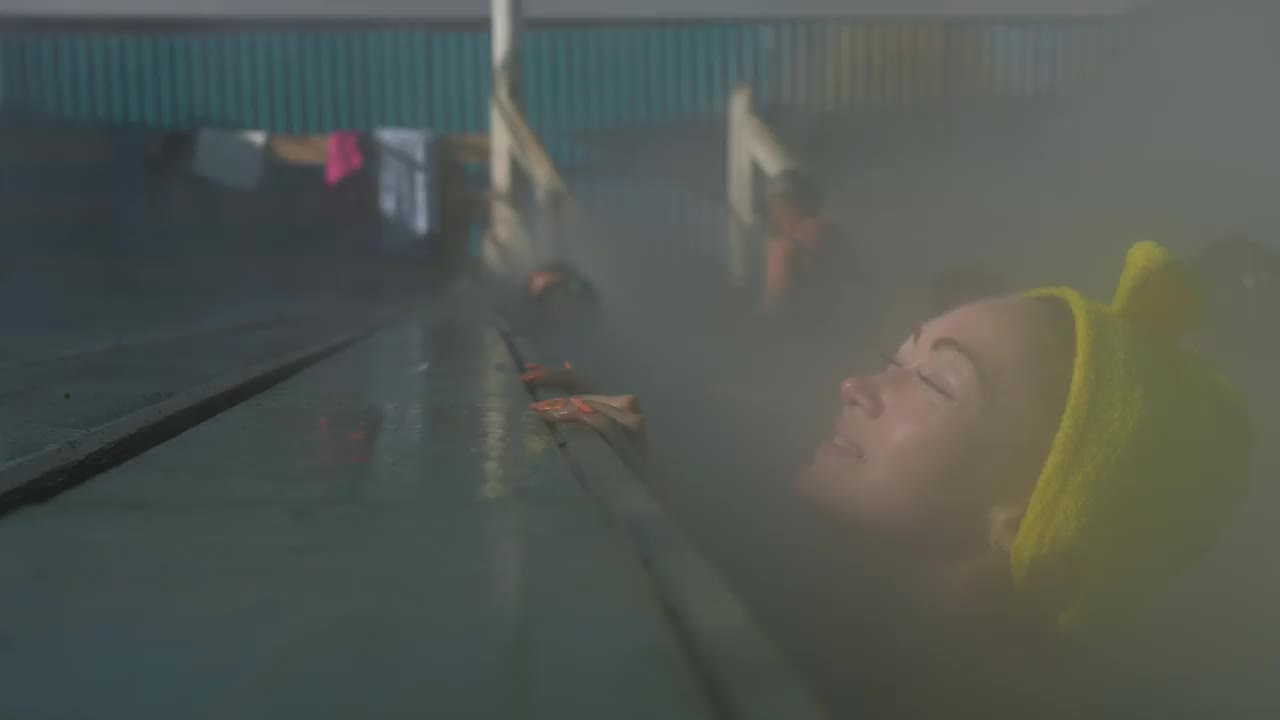 近距离的白人妇女在热盐水矿泉水浴在一个传统的温泉与软魔术粉红色照明蒸汽户外游泳。地热温泉