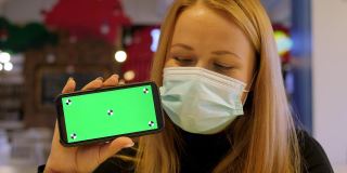 咖啡馆里，一名戴着医用口罩的女子拿着一部带有色度键的手机。
