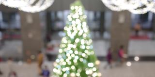 一棵挂着许多灯泡的圣诞树挂在室内。这些是用来做圣诞装饰的。模糊的背景是人们进入或离开建筑。的焦点。在看。在屏幕的中心是一棵绿色的圣诞树。