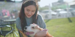 快乐在一起，有吸引力的亚洲女性年轻的成年女性喜欢与可爱的柯基狗玩，日落在室外草地后院