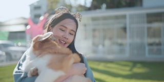 快乐在一起，有吸引力的亚洲女性年轻的成年女性喜欢与可爱的柯基狗玩，日落在室外草地后院