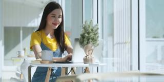 年轻有吸引力的亚洲女性穿着休闲的衣服，手使用智能手机和笔记本电脑设备交流社交在咖啡馆餐厅坐在柜台旁边的大窗户日光
