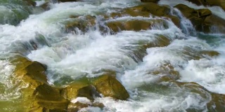 山间河流，清澈的绿松石水瀑布般从湿卵石间倾泻而下，泛着厚厚的白色泡沫。