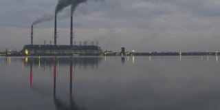 燃煤电厂的高管与黑烟快速移动污染大气在夜间与倒影在湖水。日到夜的时间推移过渡。