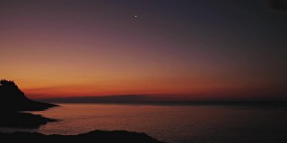 一个人的剪影看着月亮和星星在海洋的地平线上。