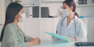 亚洲专科女医生向小女孩病人讲解诊断。专业女医生佩戴口罩，使用笔记本电脑，并在预约就诊时向住院的患者提供治疗方案。