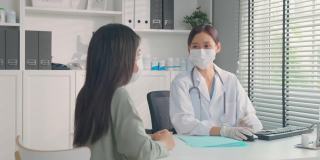 亚洲专科女医生向小女孩病人讲解诊断。专业女医生佩戴口罩，使用笔记本电脑，并在预约就诊时向住院的患者提供治疗方案。