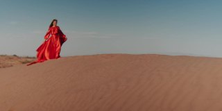 一个穿着红色裙子的亚洲女人在沙丘上跳舞