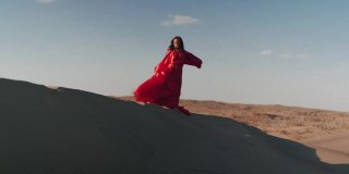 一个穿着红色裙子的亚洲女人在沙丘上跳舞