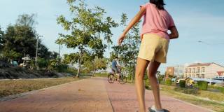 快乐的亚洲儿童，在阳光照耀下，在小路上一起骑自行车和滑板，健康的生活理念。