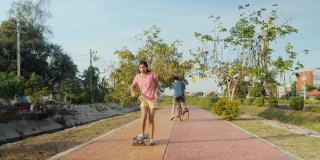 快乐的亚洲儿童，在阳光照耀下，在小路上一起骑自行车和滑板，健康的生活理念。