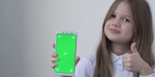 一名身穿白色校服的女学生用绿色屏幕模拟手机、手机、电话。绿屏智能手机的色度键设置为广告。教育、科技、小玩意和孩子
