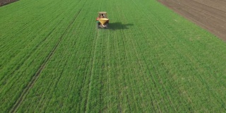 鸟瞰图在拖拉机上播撒肥料在农田上与年轻的谷物栽培