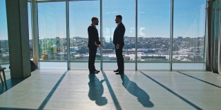 握手。商务人士的全身肖像。穿着优雅西装的男企业家们在现代化的办公室里开会，谈论生意。剖面视图。城市全景窗口的视图